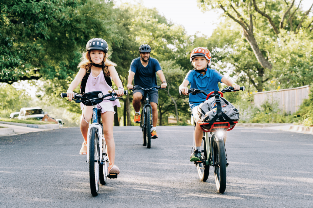 woom2school Ein Mädchen, ein Junge und im Hintergrund ein Erwachsener radeln auf woom Bikes
